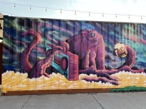 Street mural with large pink creature against a blue background in downtown Witchita Ksnsas